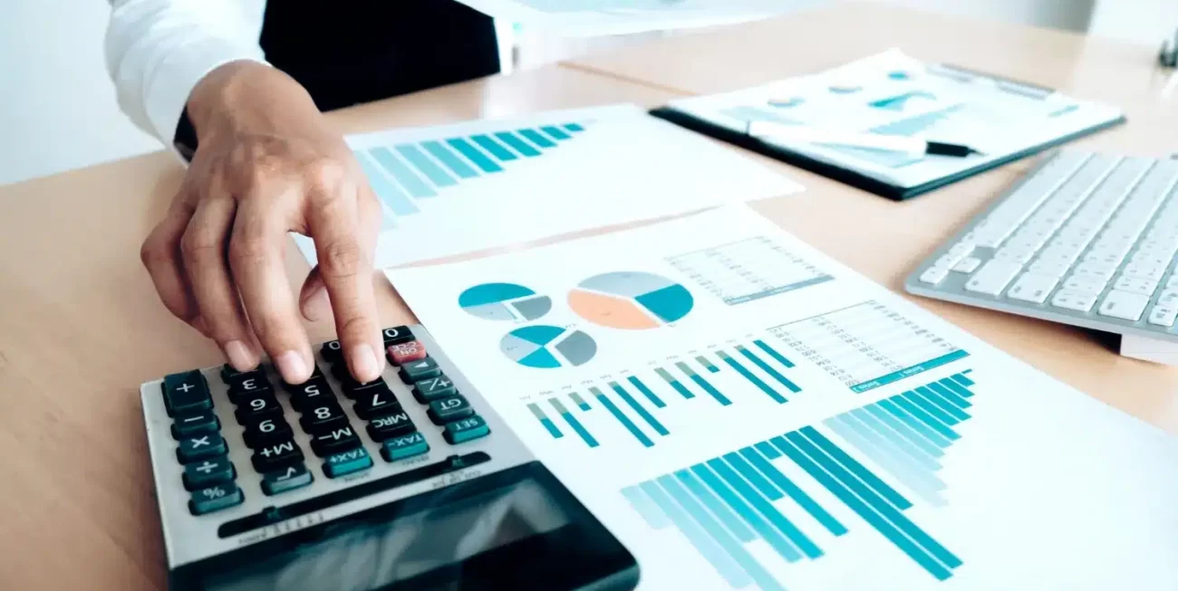 Mano usando una calculadora sobre una mesa con gráficos y documentos financieros.