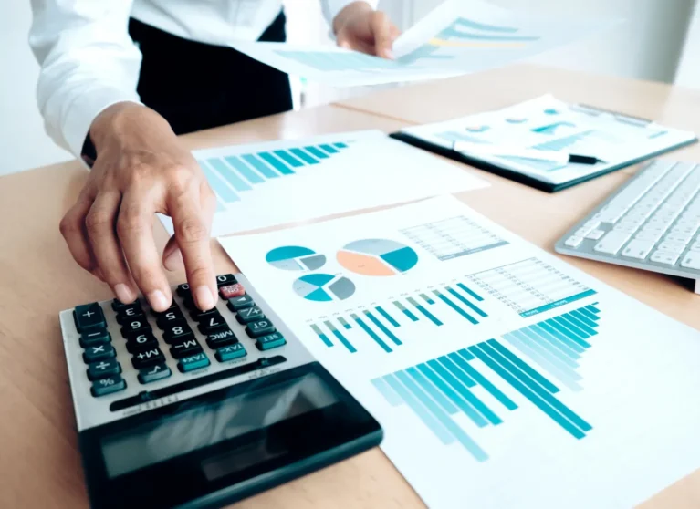 Mano usando una calculadora sobre una mesa con gráficos y documentos financieros.
