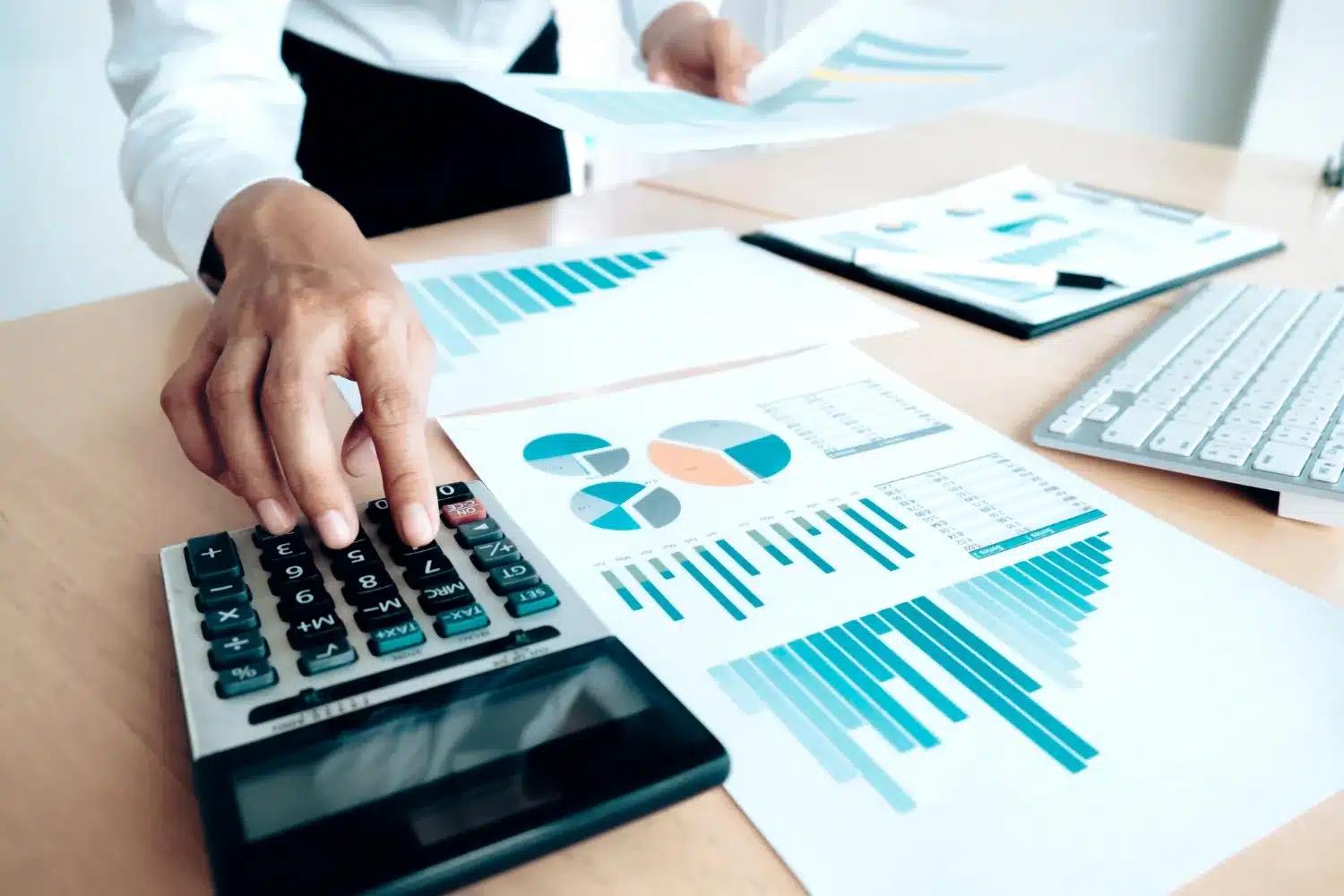 Mano usando una calculadora sobre una mesa con gráficos y documentos financieros.